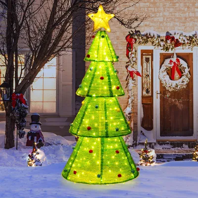 A lit-up Christmas tree decoration stands in the snow outside a house decorated for the holidays.