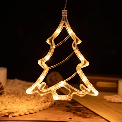 A lit-up Christmas tree decoration hangs against a dark background, with a textured mat and wooden surface in the foreground.