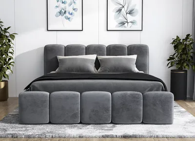 A modern bedroom setting with a gray upholstered bed, pillows, and two potted plants.