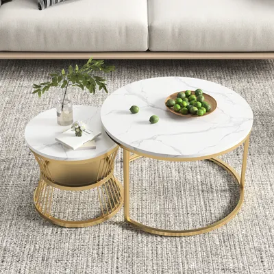Two nesting coffee tables with marble-look tops and gold metal frames are placed on a rug in front of a sofa.