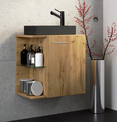 A modern bathroom vanity with a black sink and faucet, wooden cabinet, and decorative branches in a vase.
