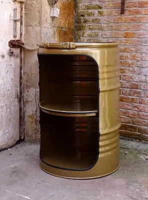 A modified metal drum with shelves, placed outdoors against a brick wall and concrete floor.