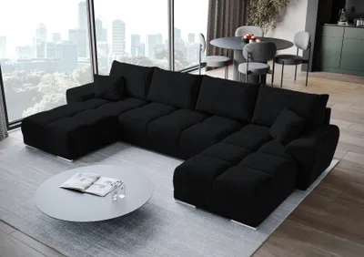 A modern living room with a large black sectional sofa, a round coffee table, and dining chairs in the background.