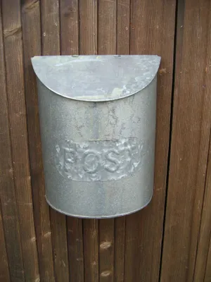 A galvanized metal mailbox is mounted on a wooden fence.
