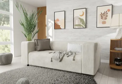 A modern living room scene with a beige corduroy sofa, decorative pillows, a throw blanket, a large potted plant, and artwork on the wall.
