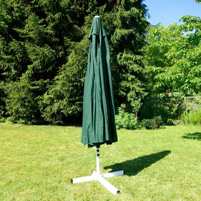 A closed green patio umbrella stands on a grassy lawn in front of trees.
