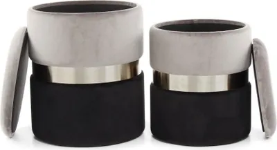 Two cylindrical ottomans are shown side-by-side against a white background. The ottomans have a two-tone design, with a gray velvet top and a black base, separated by a silver band. One ottoman's lid is slightly ajar.