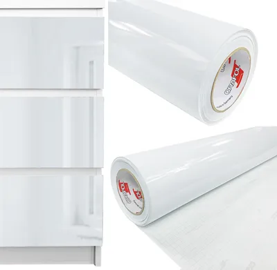 A roll of white, high-gloss furniture film is shown next to a section of white, high-gloss furniture with drawers.