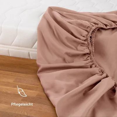 A close-up of a pink fitted sheet draped over a mattress, with a wooden floor in the foreground.