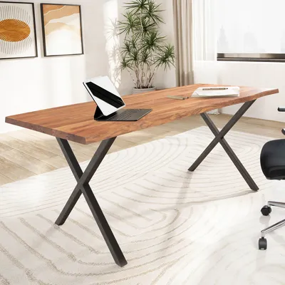 A modern home office setup featuring a live-edge wooden desk with black X-shaped legs, a tablet, and a plant in the background.