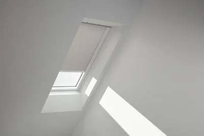 A skylight window with a gray roller blind partially drawn, set against a white ceiling and wall.