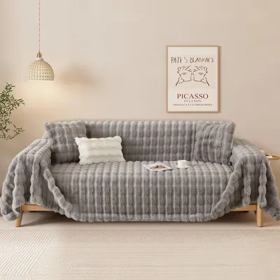 A cozy living room scene with a plush gray sofa covered in a soft blanket, featuring a framed art print on the wall and a pendant light.