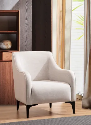 A light-colored armchair sits in a room with wooden furniture and curtains.