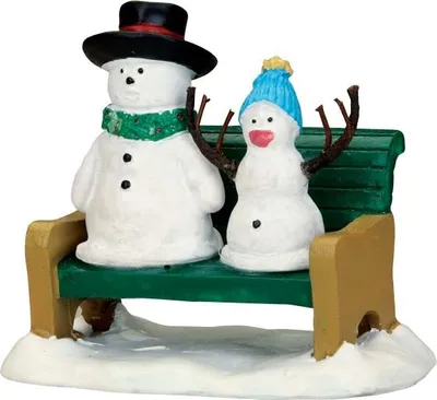 Two snowmen sitting on a park bench in the snow.