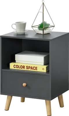 A dark gray nightstand with a drawer and an open shelf, featuring a cup and a decorative terrarium on top, and two books inside the shelf. The nightstand is supported by four wooden legs.
