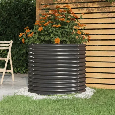 A dark gray corrugated metal planter filled with orange flowers sits on a patio next to a wooden fence and a green lawn.