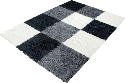 A shaggy rug with a checkered pattern of black, white, and gray squares, laid out on a white background.