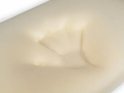 A close-up view of a cream-colored memory foam pillow with an indentation, suggesting it has been pressed.