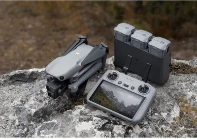A DJI Air 3 drone, its controller, and a battery charging hub are arranged on a rocky surface with a blurred natural background.