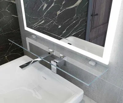 A close-up view of a modern bathroom sink with a chrome faucet and a clear glass shelf mounted above it, reflecting the illuminated mirror.