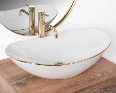 A close-up shot of a white oval basin with a gold rim and a gold faucet, placed on a wooden surface.