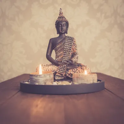 A Buddha statue with two lit candles on a tray, placed on a wooden surface.