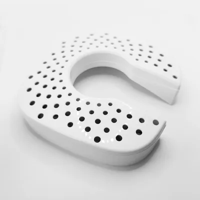 A white U-shaped object with many small holes, placed on a white surface.