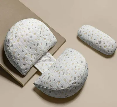 Three pregnancy pillows are arranged on a light brown surface, with one pillow partially on a beige background.