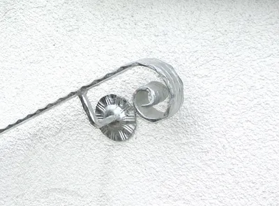 A close-up view of a metal handrail component with a scroll design, mounted on a textured wall.