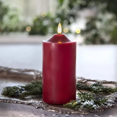 A red LED candle with a flame sits on a decorative tray with pine branches.