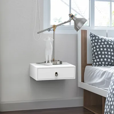 A white floating nightstand with a drawer next to a bed with a polka dot pillow.