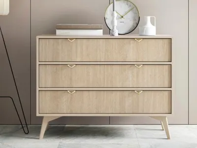 A modern beige dresser with gold handles sits in a room with a floor lamp and a clock on top.