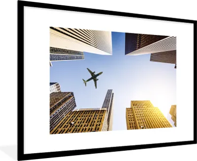 Produktbild von MuchoWow® Gerahmtes Poster Flugzeug zwischen den Wolkenkratzern 90x60 cm - Poster mit Schwarzem Bilderrahmen Wandposter Rahmen Foto Bilder - Wanddekoration - Fotos