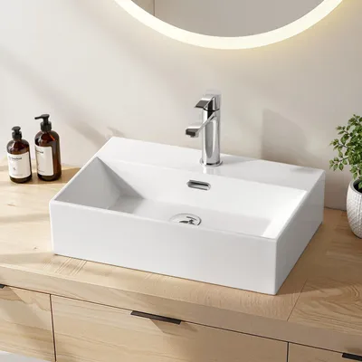 A white ceramic vessel sink with a chrome faucet is shown on a light wood vanity.