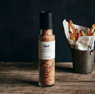 A bottle of chili blend salt next to a bucket of french fries on a wooden table.