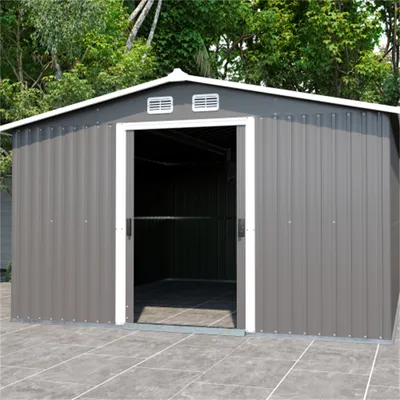 A gray metal shed with an open door, set on a paved patio with trees in the background.