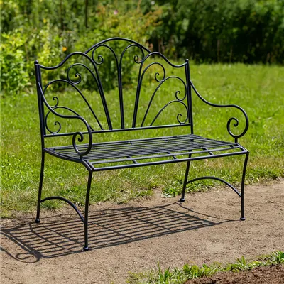 A black metal garden bench sits on a dirt path in a grassy area with trees in the background.