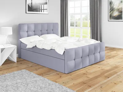 A bedroom scene with a gray boxspring bed, white bedding, a white nightstand, and a window with curtains in the background.