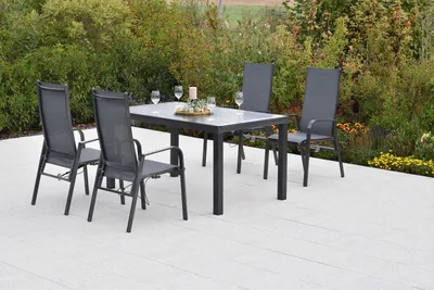 An outdoor dining set with a table and four chairs on a patio, surrounded by greenery.