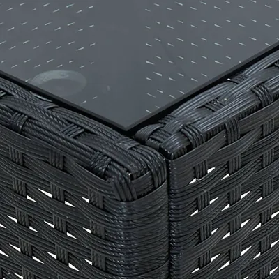 A close-up view of the corner of a black rattan garden table with a glass top.