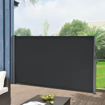 A dark gray retractable side awning is extended on a wooden deck, providing privacy and wind protection. The background shows a green lawn and trees.