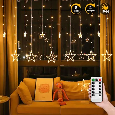 A living room scene with star-shaped string lights hanging in a window, a couch, and a framed picture.