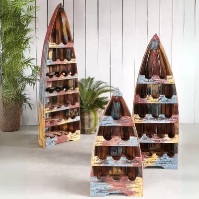 Three wooden wine racks shaped like boats are displayed in front of a white wooden wall, with plants in the background.