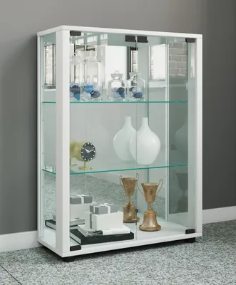 A white glass display cabinet with shelves, filled with decorative items, standing against a gray wall.