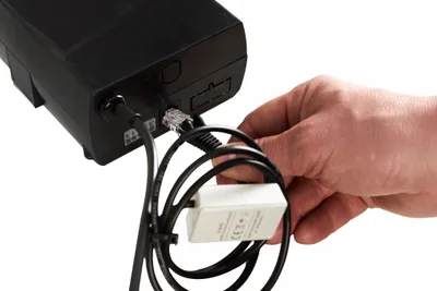 A hand is shown connecting a cable to a black electronic device.