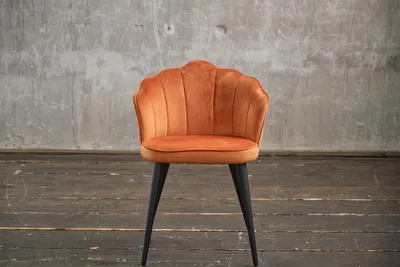 An orange velvet chair with black legs is shown against a concrete wall and wooden floor.