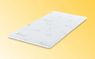 A white mattress topper with a subtle pattern of cartoon animals is shown on a gradient yellow background.