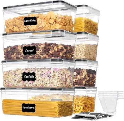 A stack of clear plastic food storage containers filled with various dry goods like cereal, pasta, and corn flakes. Each container has a black label with white text indicating its contents.