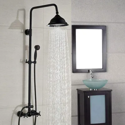 A black vintage-style shower system with a showerhead and handheld showerhead is shown in a bathroom setting. A vanity with a glass sink and a mirror are visible in the background.