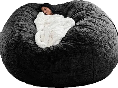 A woman is relaxing on a large, dark gray beanbag chair, covered with a white blanket.